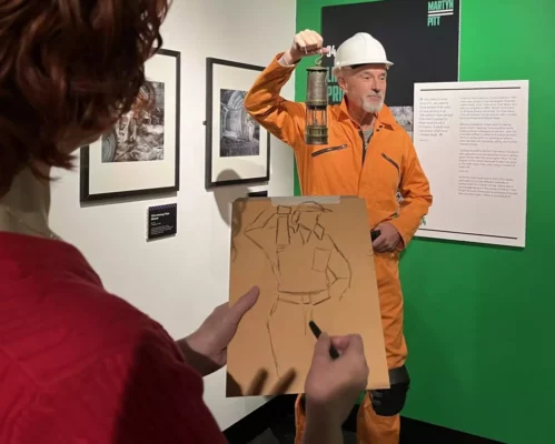 A man dressed as a coal miner poses to be drawn in the Adult Art Workshops