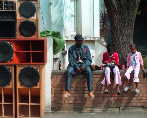 Family sitting on a wall beside a soundsystem at Notting Hill Carnival 2014
